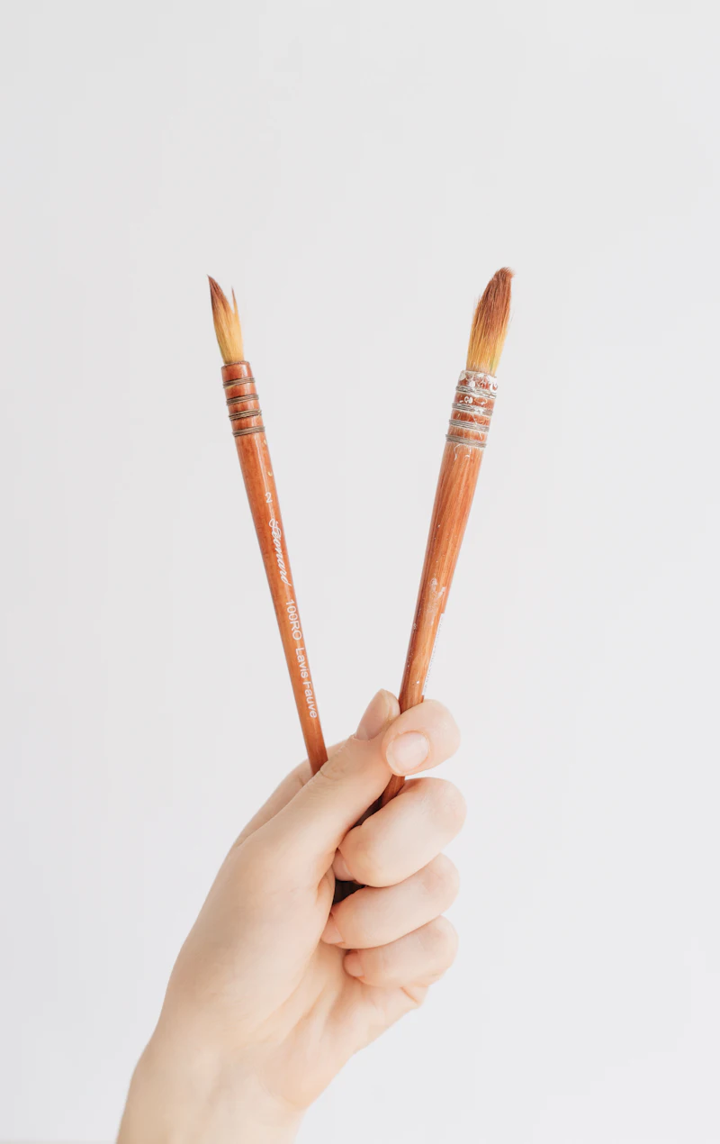 A hand holding two wooden paintbrushes