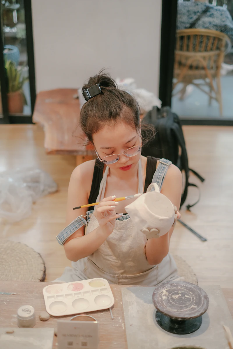 A girl in an apron painting a small white figure at a table