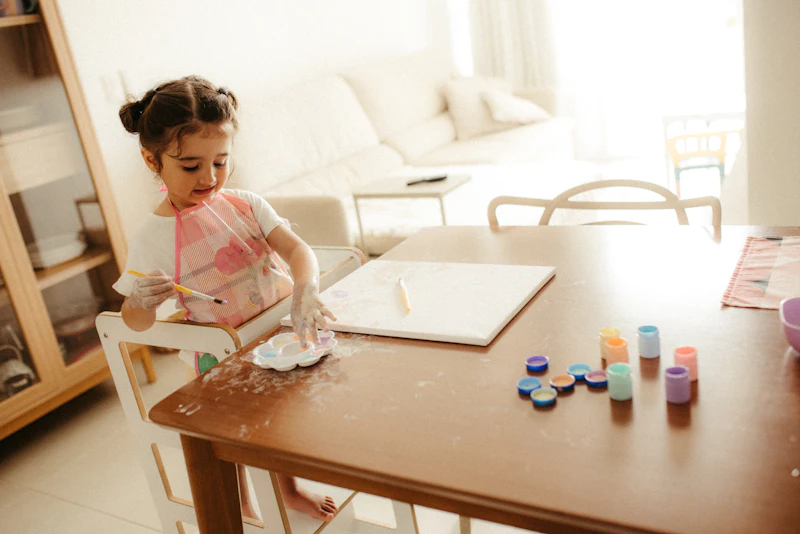 A toddler painting at a wooden table in a bright, quiet living room